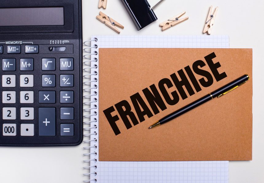 Na pulpicie kalkulator, długopis i spinacze do bielizny obok notesu z napisem FRANCZYZA. Pomysł na biznes. Widok z góry