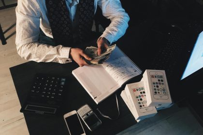 Businessman organizing finances with tech devices and cash on desk.