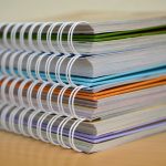 A colorful stack of spiral-bound notebooks neatly placed on a wooden desk. Ideal for educational themes.