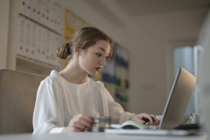Focused young woman working remotely on a laptop in a modern office.