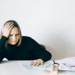 Woman in black sweater stressed with financial paperwork, overwhelmed at white table.