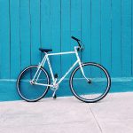 white road bike leaning on teal wooden wall during daytime