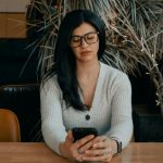 woman in white cardigan holding black smartphone