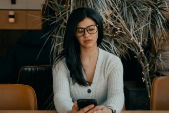 woman in white cardigan holding black smartphone