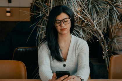 woman in white cardigan holding black smartphone