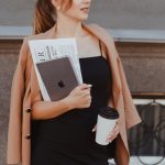 a woman in a black dress holding a coffee cup and a book
