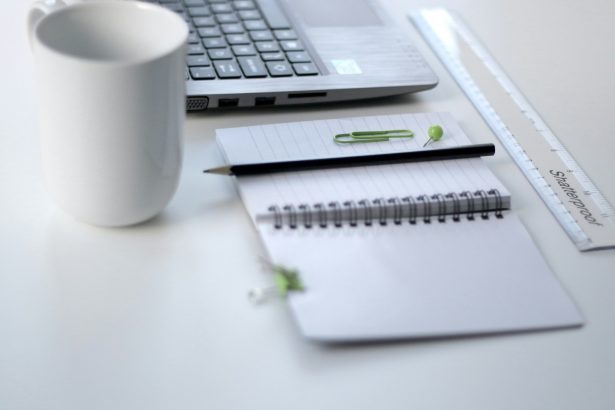 black pencil on ruled notepad beside white ceramic mug and gray laptop computer