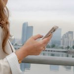 Woman checks her phone with cityscape in the background.
